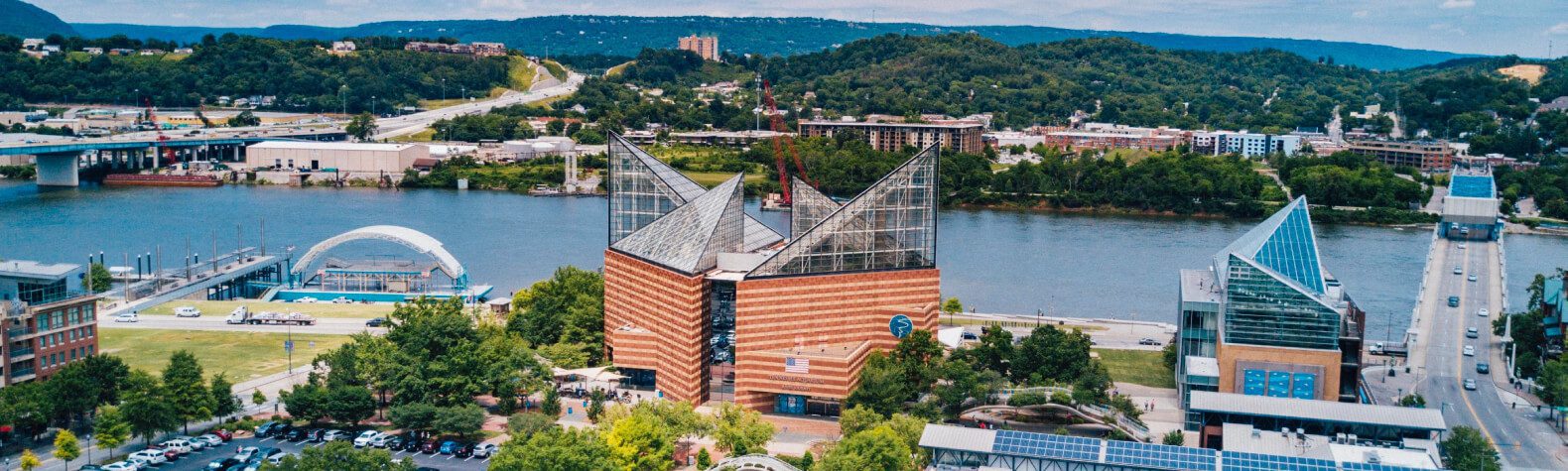Modern aquarium buildings by river with city and hills in background.