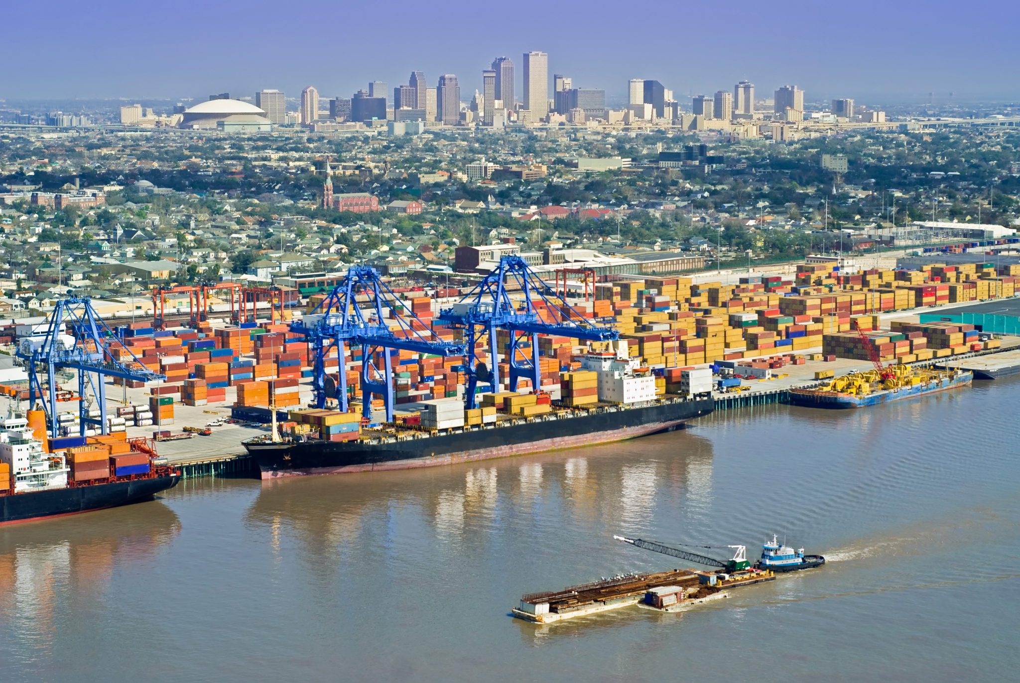 Shipping port with containers, cranes, and city skyline.
