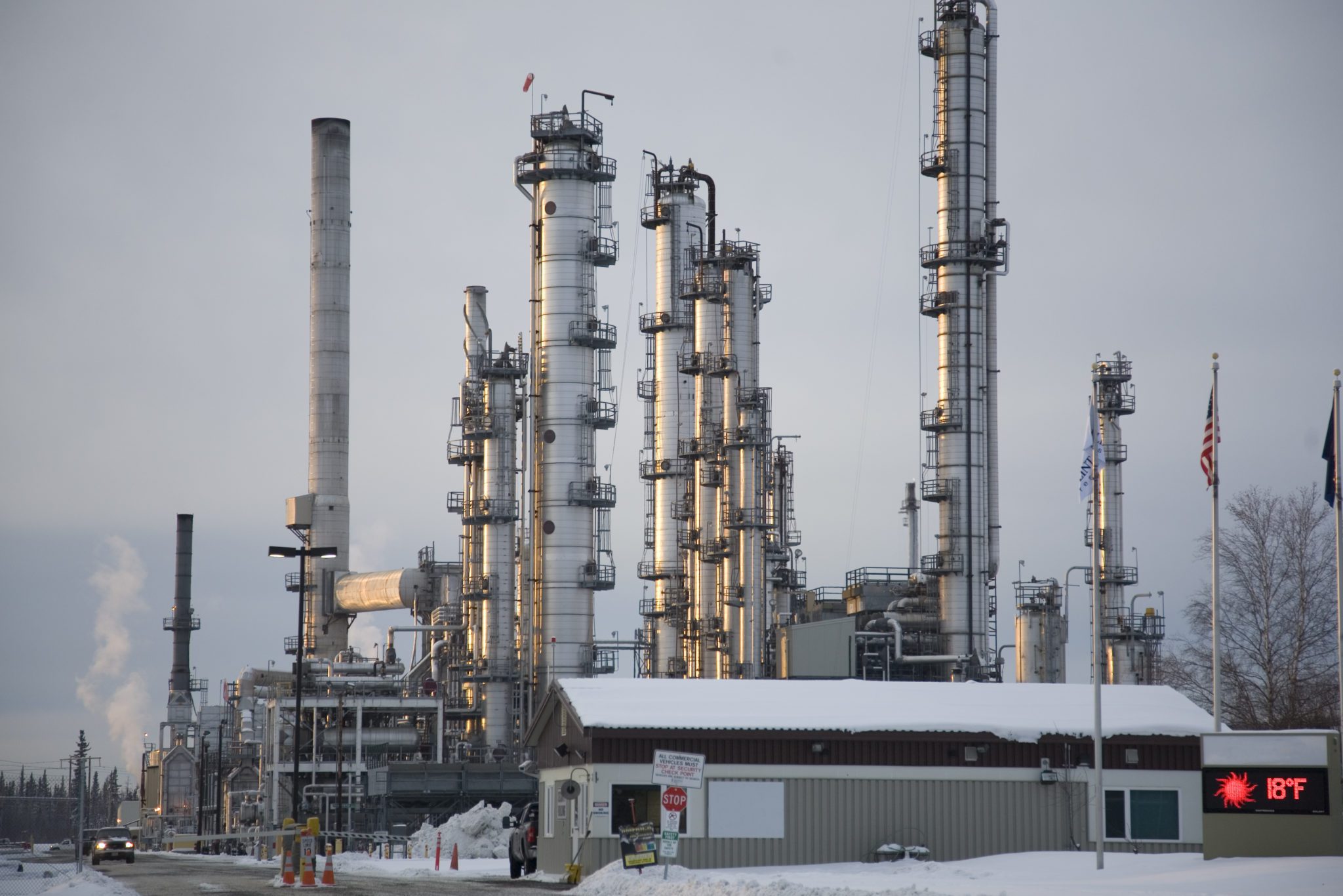 Industrial refinery plant during winter with snow-covered ground and a digital sign showing 18Β°F.
