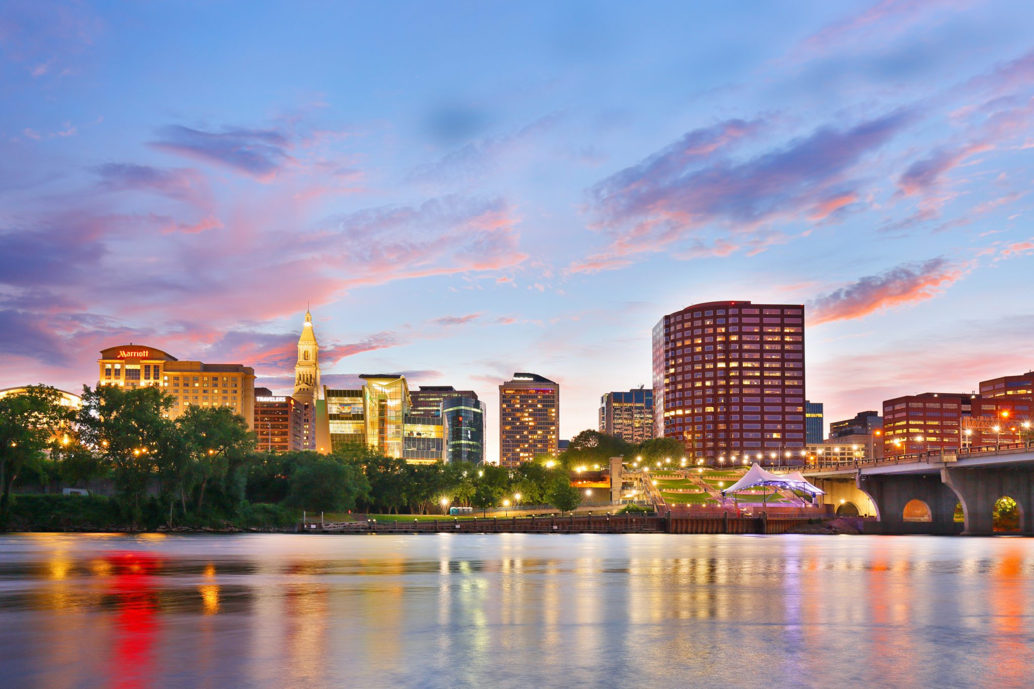 City skyline with bridge and colorful sunset reflections on river.